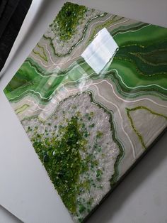 a piece of art with green and white designs on it's surface, sitting on a table