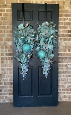 two green wreaths on the front door of a brick building with blue glass ornaments