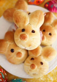 some buns shaped like teddy bears on a plate with other rolls in the background