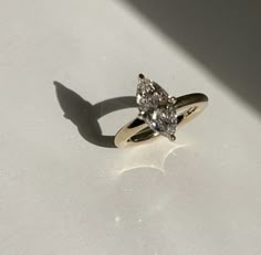 an engagement ring with two pear shaped diamonds on the side, sitting on a white surface