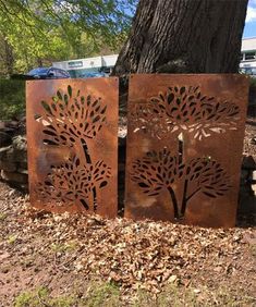 two metal art pieces sitting next to a tree