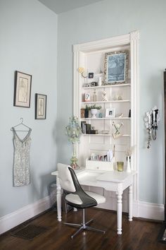 a white desk and chair in a room with blue walls, hardwood floors and pictures on the wall