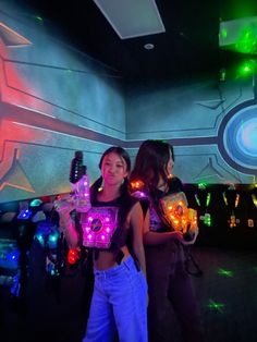 two young women standing next to each other in a room with neon lights on the walls