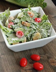 lettuce and tomato salad in a white bowl on a wooden table next to tomatoes