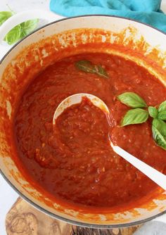 a pot filled with red sauce and basil leaves