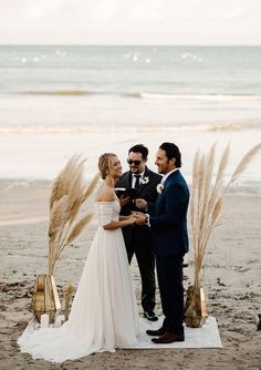 a man and woman standing next to each other on top of a sandy beach near the ocean