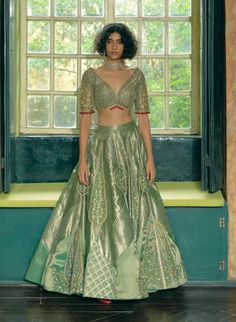 Step into timeless elegance with this classic kalidar lehenga set, crafted from emerald green silk zari tissue and jacquard silk banarasi. Featuring jharokha-inspired panels and intricate floral embroidery with zari and zardozi work, the design is enhanced with dabka, sequins, pearls, and gota texturing. The set includes a heavily embroidered elbow-sleeve blouse adorned with floral motif embroidery and pearl tassels. Complemented by a shimmering emerald green tissue dupatta with paisley embroidery, sequins, and pearl tassels, this ensemble creates a gracefully defined and sophisticated silhouette. Green Banarasi Lehenga, Tissue Silk Lehenga, Paisley Embroidery, Zardosi Embroidery, Lehenga Pattern, Elbow Sleeve, Green Silk, Floral Embroidery, Aza Fashion