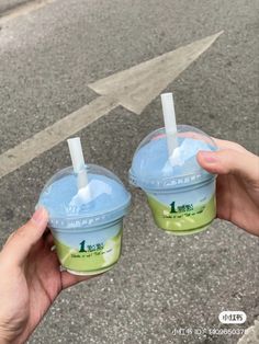 two people holding up plastic cups with straws in them on the street, one is blue and green