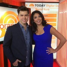 a man and woman standing next to each other in front of a tv screen with the words orange today on it