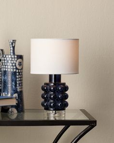 a lamp sitting on top of a glass table next to a book and vases