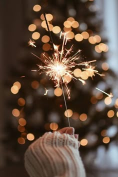 a person holding a sparkler in front of a christmas tree with lights on it