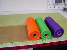 three rolls of colored fabric sitting on top of a table next to a ruler and scissors