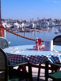 the table is set for two on the dock with boats in the water behind it