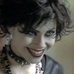 a close up of a person wearing necklaces and smiling at the camera with an evil smile on her face