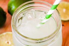 a mason jar with a green and white striped straw next to sliced lemons on a wooden table