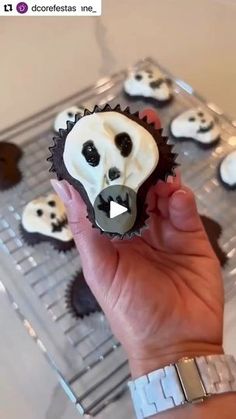 a person holding a cupcake with white frosting and black sprinkles