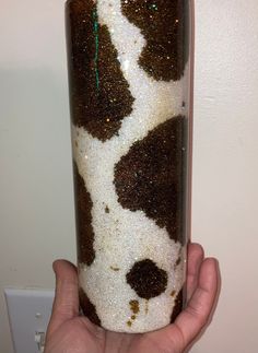 a hand holding a glass with brown and white speckles on the bottom, in front of a wall