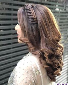 a woman with long brown hair wearing a braided hairstyle in front of a wall