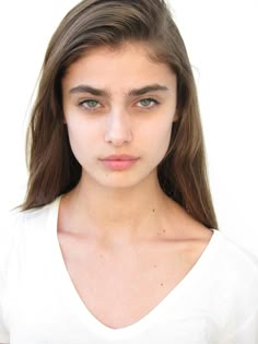 a young woman with long hair wearing a white t - shirt and looking at the camera