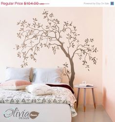 a bedroom with a tree decal on the wall and bed in front of it