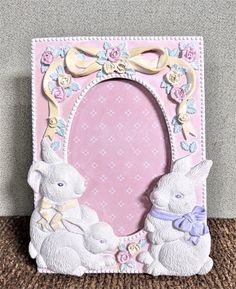 a pink frame with two white rabbits on it and a bow around the edge, sitting on a brown carpet