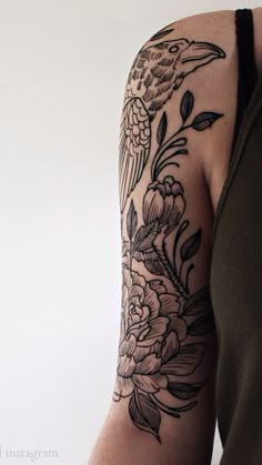 a woman's arm with a bird and flowers tattoo on her left arm, next to a white wall