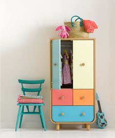 a child's wardrobe with colorful drawers and chairs next to it, in front of a white wall