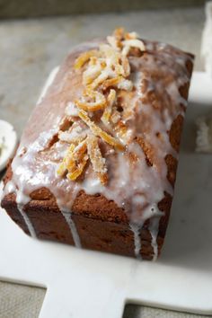 a loaf of cake with icing and nuts on top sitting on a cutting board