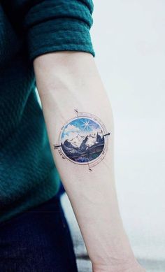 a man's arm with a compass tattoo on it and mountains in the background