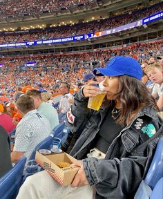 a woman sitting in the bleachers with a box of popcorn and a drink