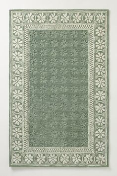 a green and white rug with an intricate design on the bottom, in front of a white wall