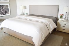 a bedroom with a bed, nightstands and pictures on the wall behind it in shades of gray and white