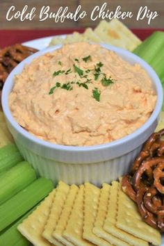 a plate with crackers, celery and pretzels next to a bowl of dip