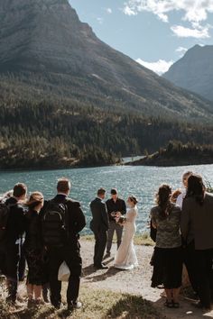 a group of people standing next to each other near a body of water with mountains in the background