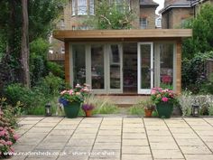 a garden with potted plants and flowers in front of a building that is surrounded by trees