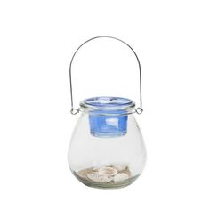 a glass jar filled with sand and water on top of a white background, next to a blue lid