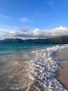 the beach has waves coming in from the water and mountains in the distance with blue sky