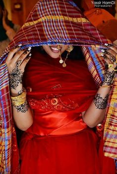 a woman in a red dress holding her hands up to her face with henna tattoos on