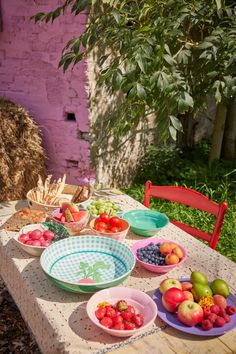 a wooden table topped with plates and bowls filled with fruit next to a pink building