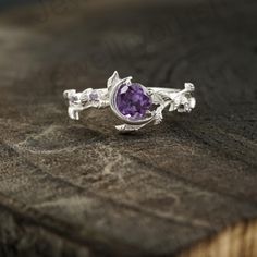 a ring with an amethorate stone and leaves on the side sitting on top of a piece of wood