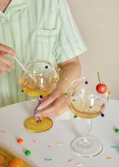 a person holding a spoon over two glasses filled with liquid and sprinkles