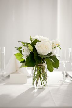 a vase filled with white flowers sitting on top of a table next to wine glasses