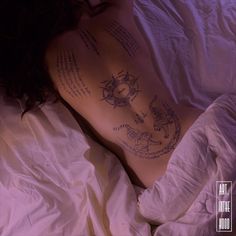 the back of a woman laying in bed with tattoos on her stomach and chest,