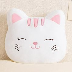 a white cat pillow sitting on top of a bed