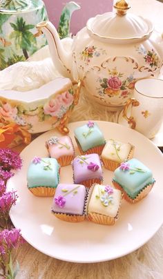 some cupcakes are sitting on a plate next to a teapot and flowers