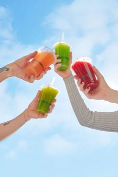 four people are holding up drinks in their hands against a blue sky with white clouds