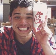 a young man holding up a cup with a drink in it's hand and smiling at the camera