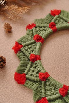 a crocheted christmas wreath with red flowers and pine cones on the floor next to it