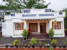 a small white house with brown shutters and potted plants on the front lawn