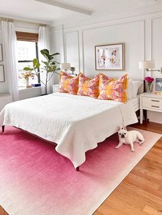 a white bed with pink and yellow pillows on top of it next to a wooden floor